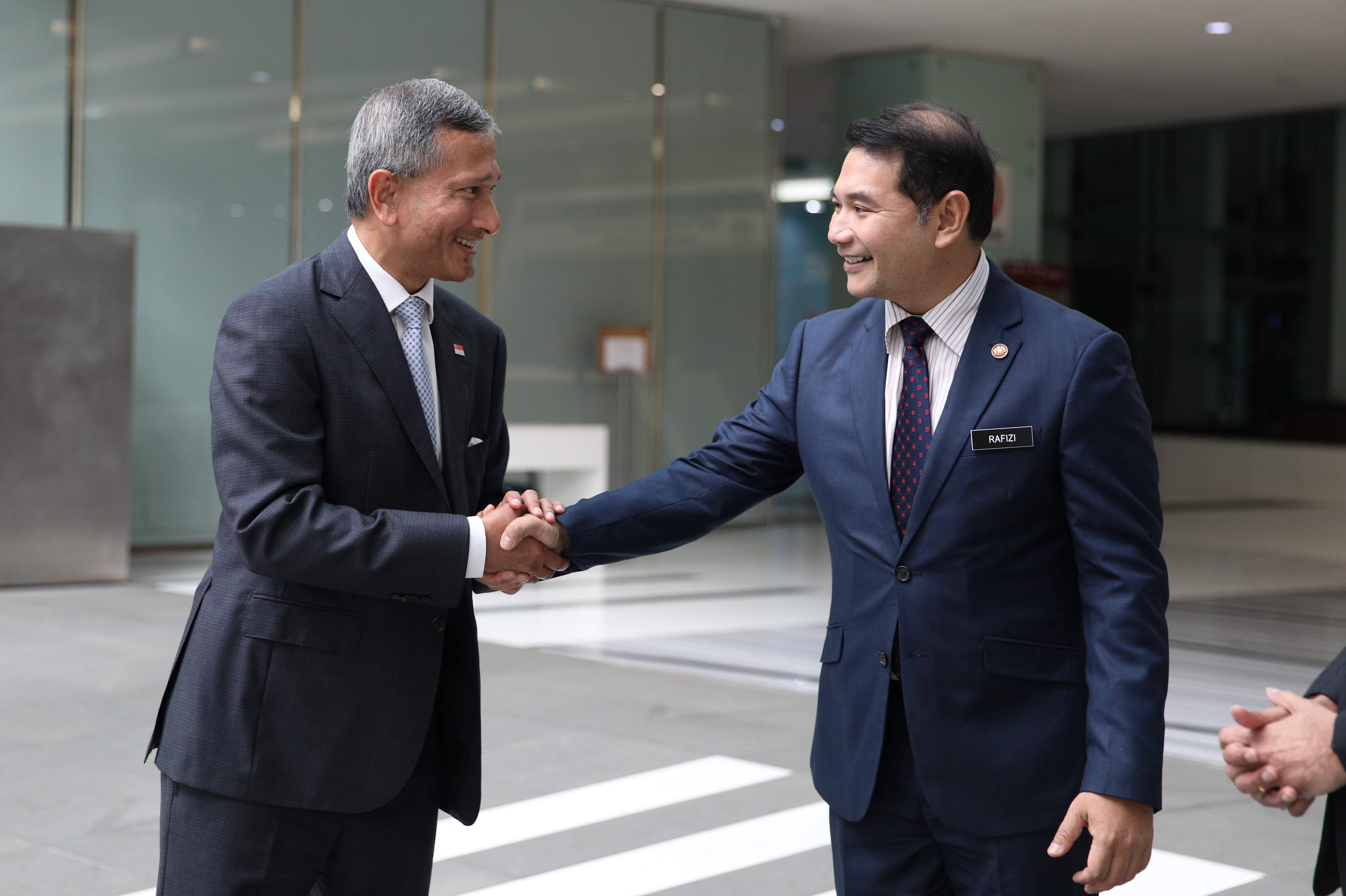 Two men in suits shaking hands; Rafizi's name tag is visible.